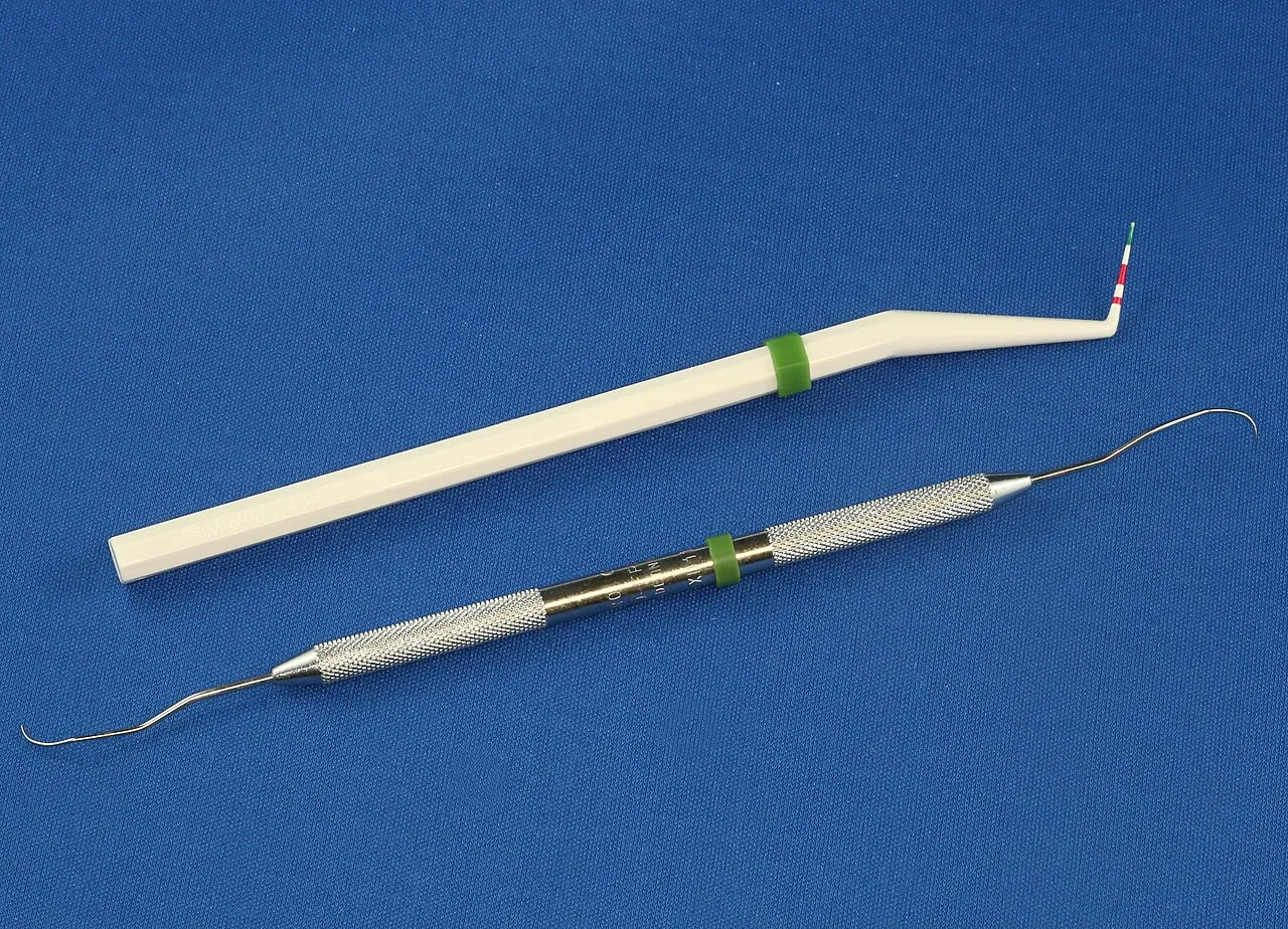 A plastic periodontal probe with color-coded markings above a double-ended metal explorer on a blue background