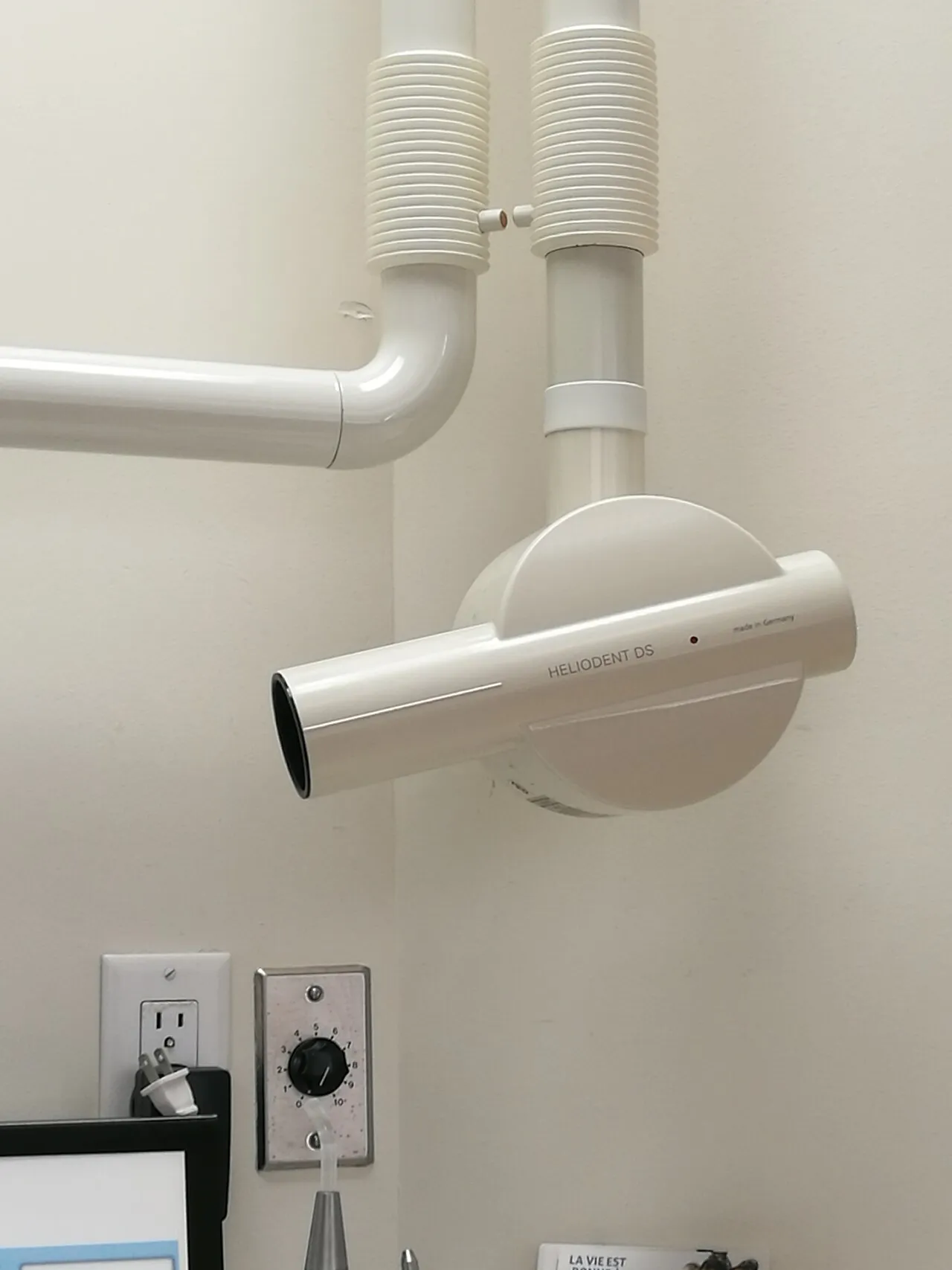 A wall-mounted intraoral x-ray tube head on an extension arm with a round open-ended PID, with the exposure timer mounted on the wall below